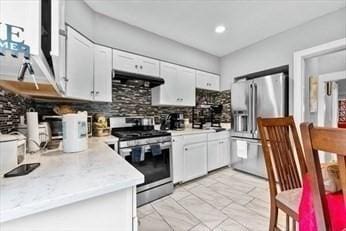 kitchen featuring under cabinet range hood, white cabinetry, light countertops, appliances with stainless steel finishes, and decorative backsplash