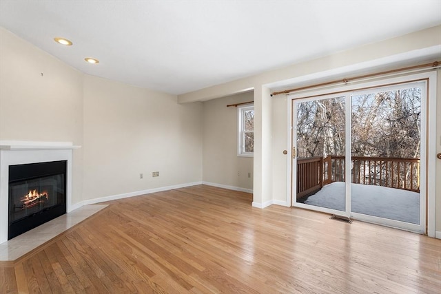 unfurnished living room with light wood-style floors, a fireplace with flush hearth, and baseboards