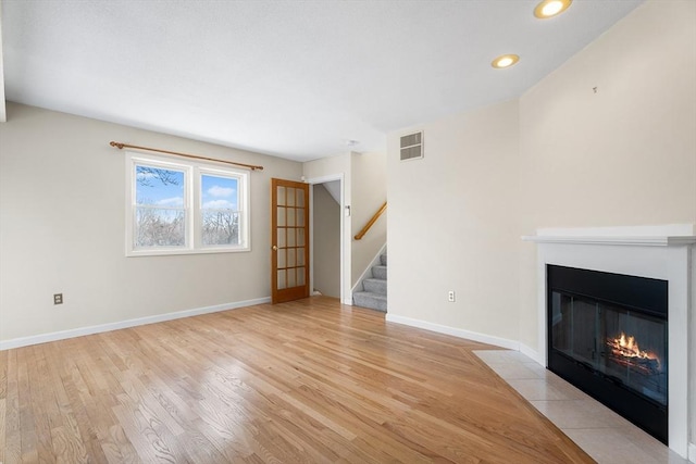 unfurnished living room featuring visible vents, stairway, a fireplace with flush hearth, light wood-style floors, and baseboards