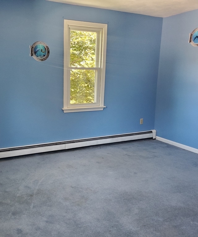 carpeted empty room featuring a baseboard heating unit