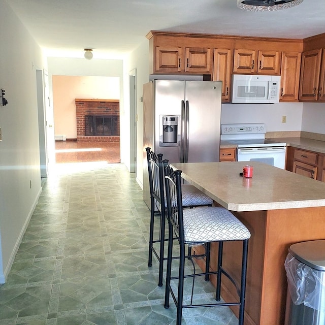 kitchen with baseboard heating, a kitchen breakfast bar, white appliances, and a brick fireplace