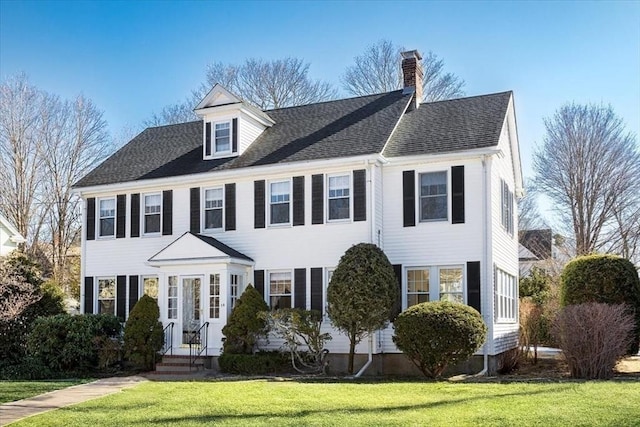 colonial home featuring a front lawn, a chimney, and a shingled roof