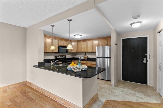 kitchen with dark stone counters, kitchen peninsula, hanging light fixtures, and appliances with stainless steel finishes