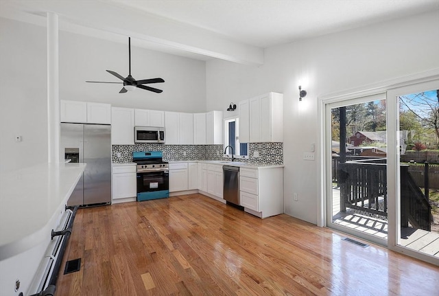 kitchen with decorative backsplash, a ceiling fan, appliances with stainless steel finishes, a sink, and light wood-style flooring