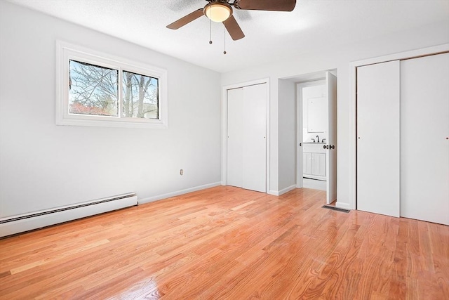 unfurnished bedroom with baseboard heating, light wood finished floors, two closets, baseboards, and visible vents