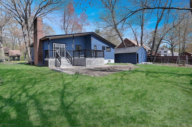 back of house featuring a chimney, a lawn, a wooden deck, fence, and an outdoor structure