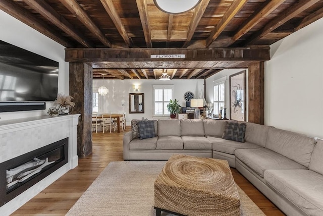 living area featuring wood ceiling, beam ceiling, wood finished floors, and a glass covered fireplace