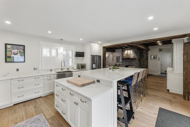 kitchen featuring light wood-style flooring, a sink, white cabinetry, stainless steel refrigerator with ice dispenser, and a center island