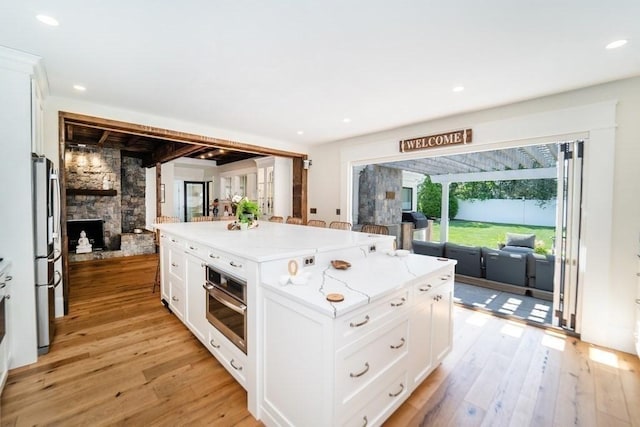 kitchen featuring stainless steel appliances, a fireplace, light wood-style flooring, and light stone counters