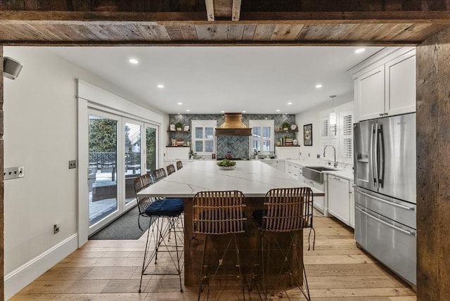 kitchen featuring a sink, white cabinetry, light wood-type flooring, stainless steel refrigerator with ice dispenser, and a center island