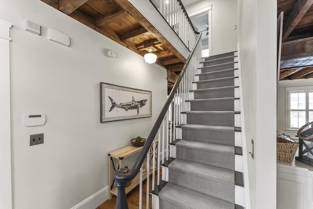 staircase featuring visible vents, wood finished floors, wooden ceiling, beamed ceiling, and baseboards