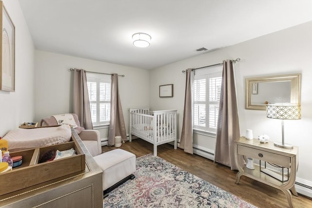 bedroom with a baseboard heating unit, multiple windows, and wood finished floors