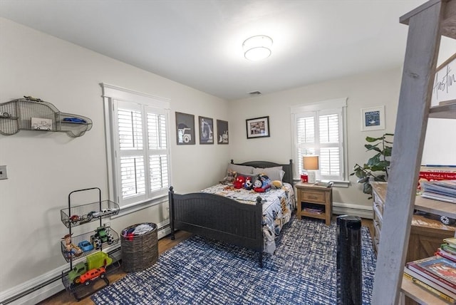 bedroom with a baseboard radiator, multiple windows, visible vents, and wood finished floors