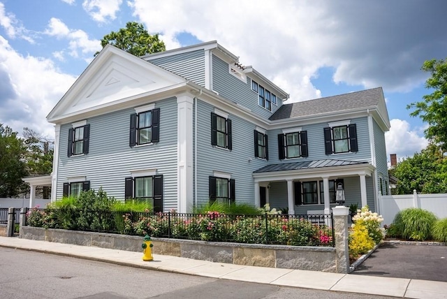 neoclassical / greek revival house featuring a standing seam roof, metal roof, a porch, and a fenced front yard