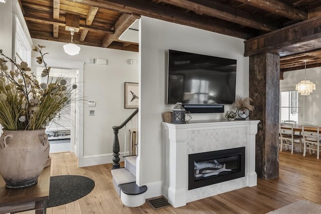 living area with a glass covered fireplace, wood ceiling, hardwood / wood-style floors, beamed ceiling, and stairs