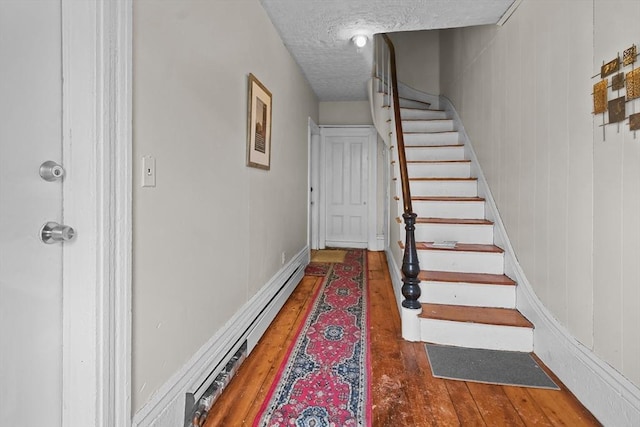 staircase with wood-type flooring, a textured ceiling, and baseboard heating