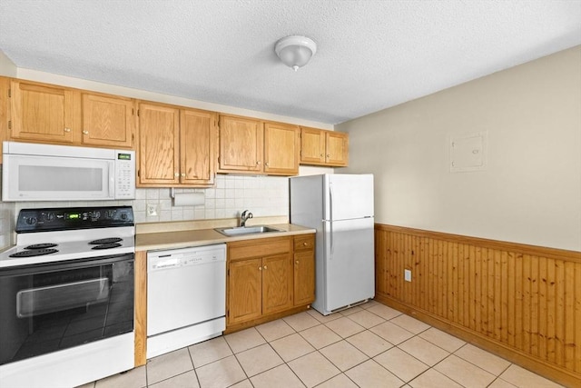 kitchen featuring wooden walls, sink, light tile patterned floors, white appliances, and a textured ceiling