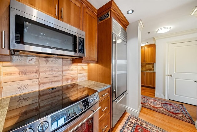 kitchen with stainless steel appliances, light stone countertops, tasteful backsplash, and wood-type flooring