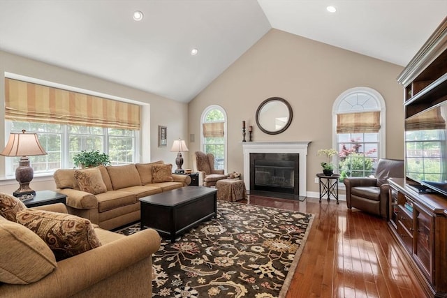 living area with high vaulted ceiling, healthy amount of natural light, a fireplace with flush hearth, wood-type flooring, and recessed lighting