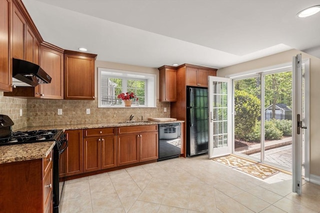kitchen featuring black appliances, under cabinet range hood, light stone counters, tasteful backsplash, and plenty of natural light