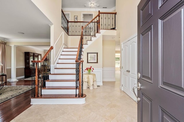 entrance foyer with ornamental molding, stairs, ornate columns, a wainscoted wall, and a decorative wall