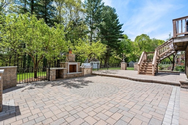 view of patio / terrace featuring an outdoor stone fireplace, stairway, fence, and view of wooded area
