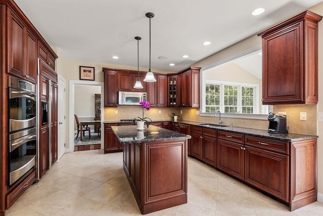 kitchen with stainless steel appliances, a sink, backsplash, decorative light fixtures, and a center island
