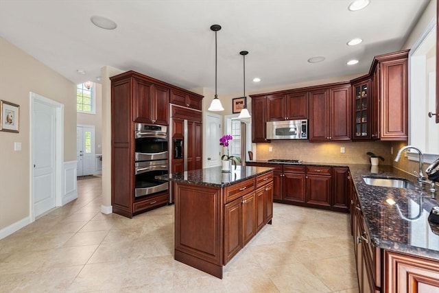kitchen featuring appliances with stainless steel finishes, a sink, dark stone countertops, glass insert cabinets, and a wainscoted wall