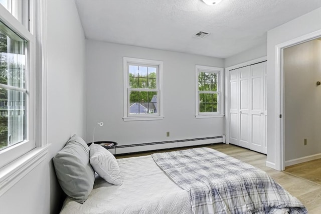 1 New Castle Rd, Ashland, MA 01721 - bedroom featuring a baseboard radiator, light wood finished floors, baseboards, a textured ceiling, and a closet