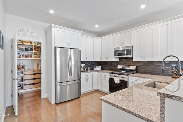 kitchen with sink, white cabinetry, stainless steel appliances, light stone countertops, and light wood-type flooring