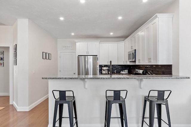 kitchen featuring stone counters, appliances with stainless steel finishes, white cabinets, and kitchen peninsula