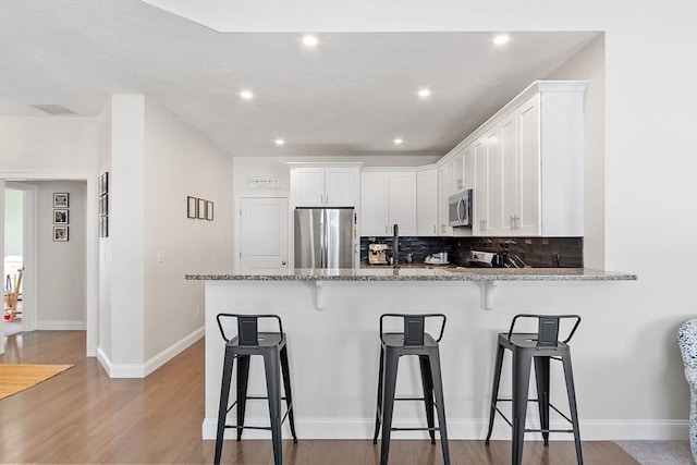 kitchen with stone counters, stainless steel appliances, kitchen peninsula, and white cabinets