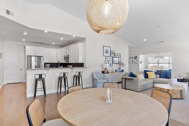 dining area with high vaulted ceiling, sink, a notable chandelier, and light wood-type flooring