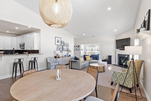 dining space featuring high vaulted ceiling, sink, light wood-type flooring, and a notable chandelier