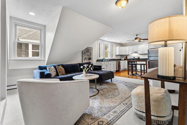 living room with baseboard heating, ceiling fan, and light wood-type flooring