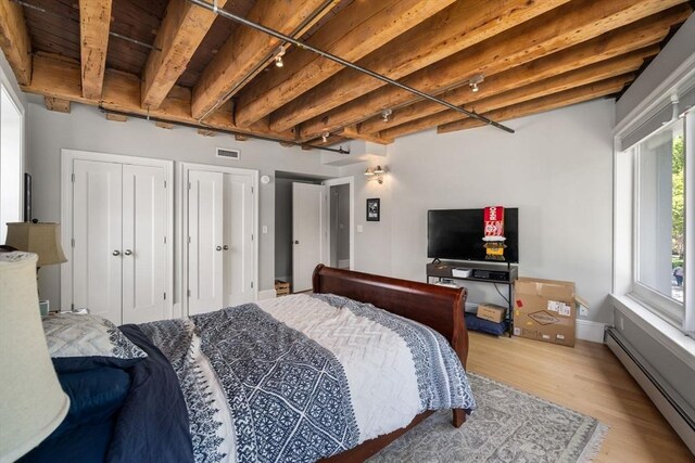 33 Commercial Wharf Unit 33A, Boston, MA 02110 - bedroom featuring a baseboard heating unit, light wood finished floors, multiple closets, wood ceiling with exposed beams, and baseboards