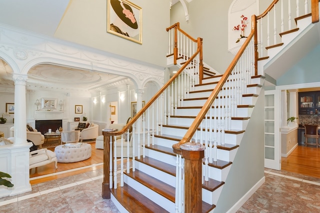 staircase with ornamental molding, a raised ceiling, a high ceiling, and decorative columns