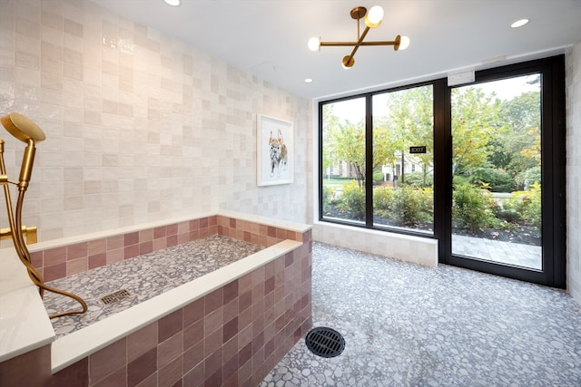 bathroom featuring tile walls, an inviting chandelier, and a healthy amount of sunlight