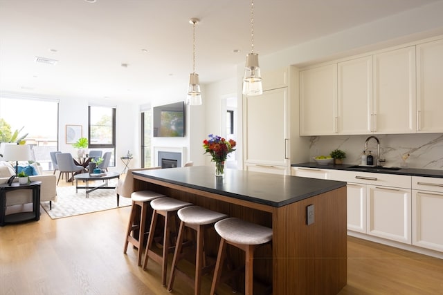 kitchen featuring light wood-type flooring, a center island, tasteful backsplash, sink, and white cabinetry