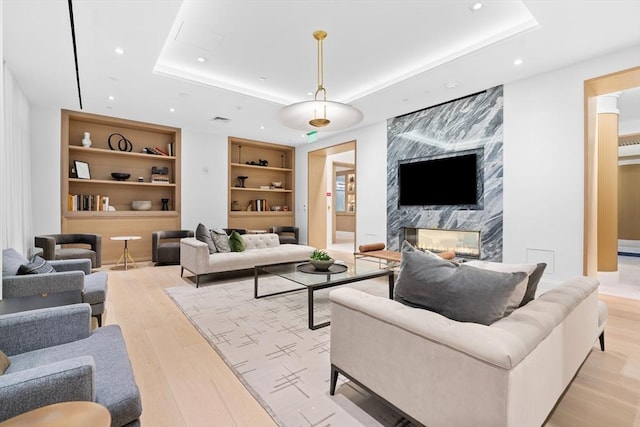 living room with light wood-style floors, built in shelves, a raised ceiling, and a high end fireplace