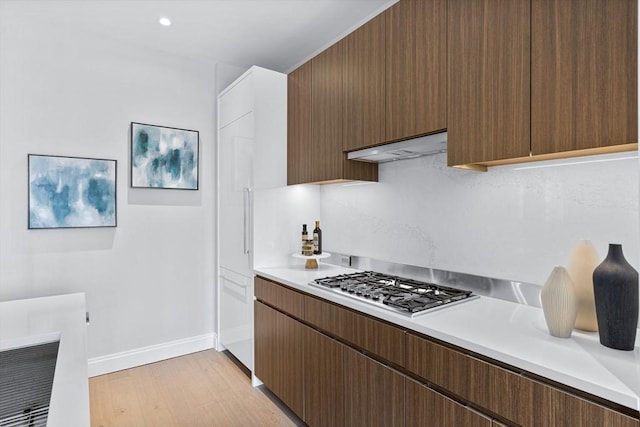 kitchen with extractor fan, baseboards, light countertops, light wood finished floors, and stainless steel gas stovetop