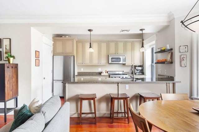 kitchen featuring appliances with stainless steel finishes, cream cabinets, a sink, ornamental molding, and a kitchen bar