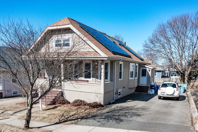 view of front of home featuring solar panels, aphalt driveway, entry steps, and roof with shingles