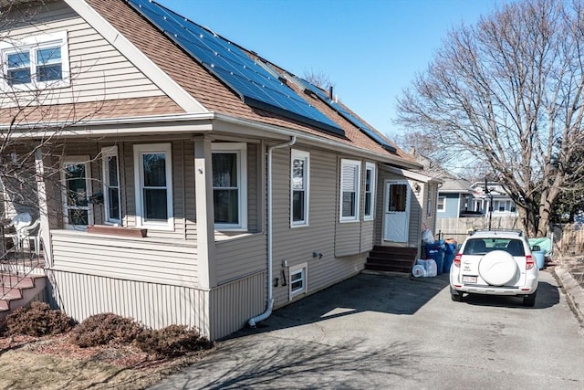 view of side of home with roof mounted solar panels, entry steps, roof with shingles, and fence