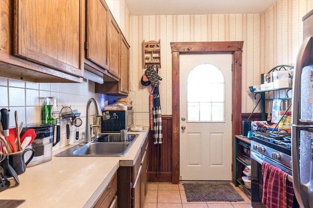 kitchen with light tile patterned floors, wallpapered walls, a sink, light countertops, and brown cabinets