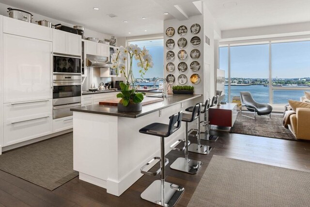 kitchen featuring a water view, white cabinetry, wall chimney exhaust hood, and dark hardwood / wood-style floors