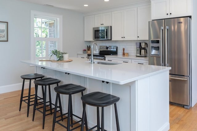 28 Marthas Rd, Edgartown, MA 02539 - kitchen featuring stainless steel appliances, light wood-style floors, white cabinetry, tasteful backsplash, and an island with sink