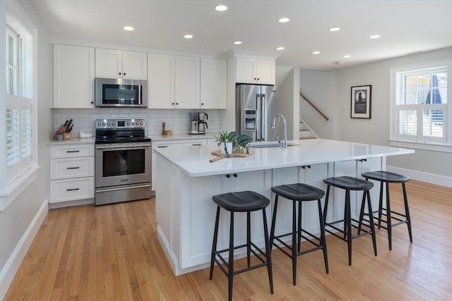 28 Marthas Rd, Edgartown, MA 02539 - kitchen featuring stainless steel appliances, light wood-style floors, a kitchen bar, white cabinetry, and backsplash