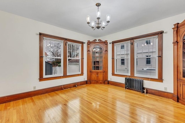 empty room featuring a chandelier, radiator heating unit, and hardwood / wood-style floors