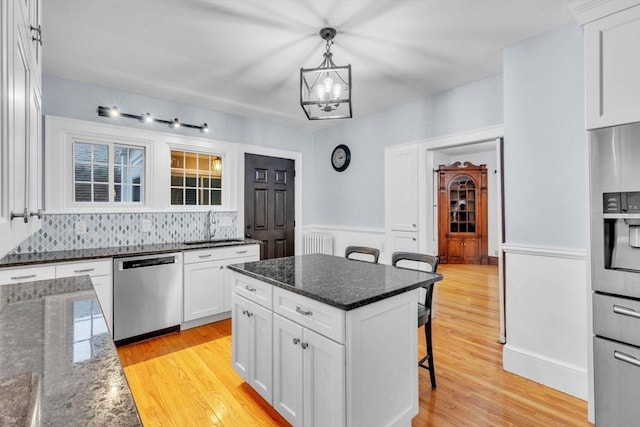 kitchen with dark stone countertops, decorative light fixtures, a kitchen bar, white cabinetry, and stainless steel appliances